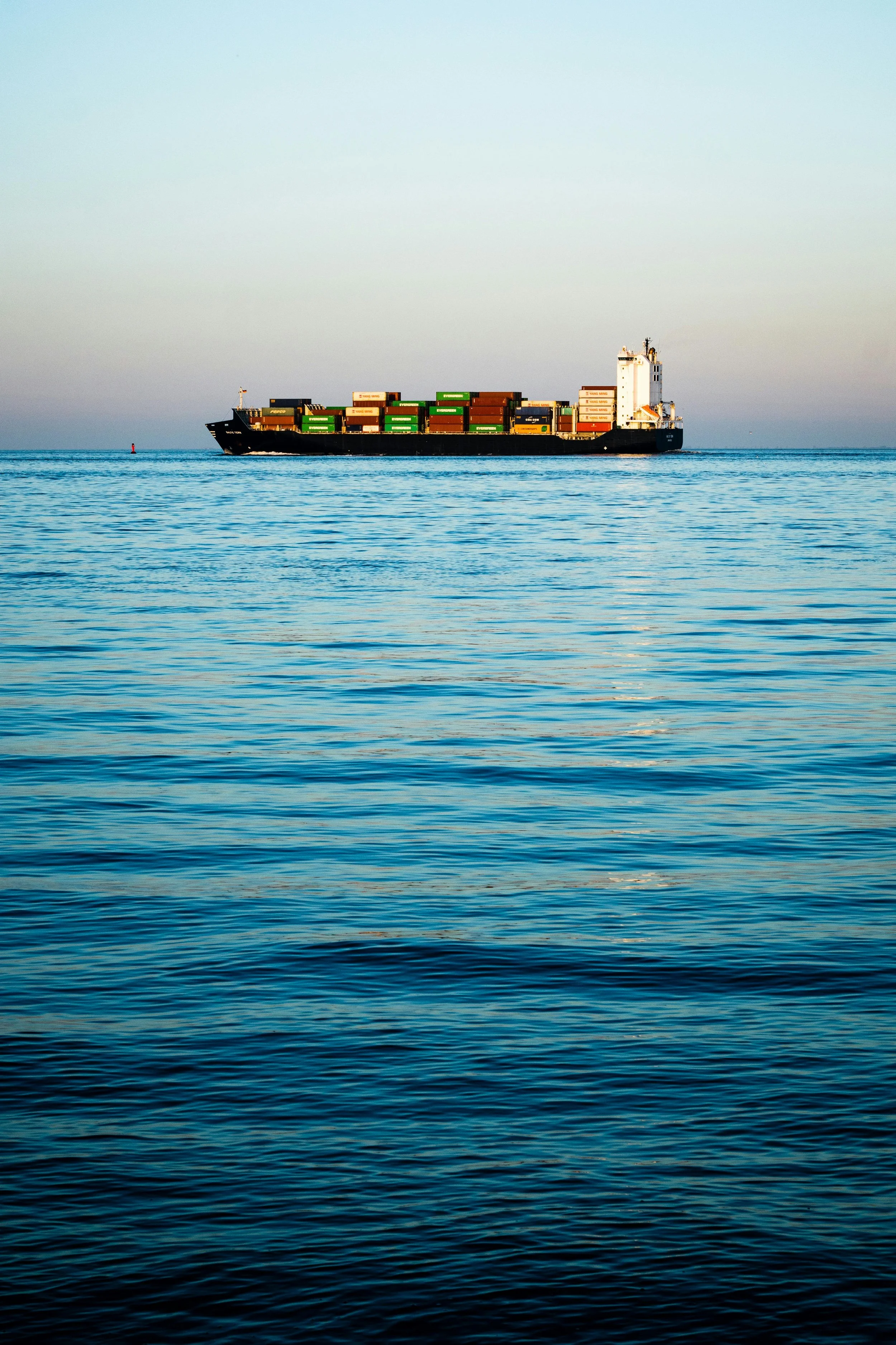 Large cargo ship sailing on calm blue ocean waters under clear sky.