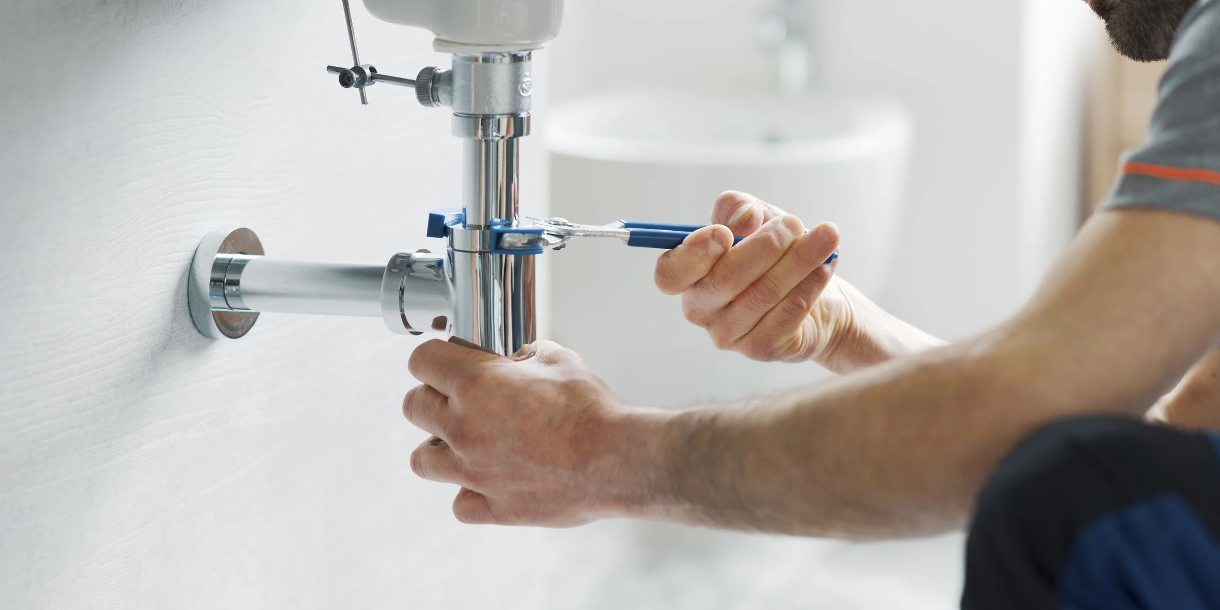 A person repairing a faucet with pliers in a bathroom.