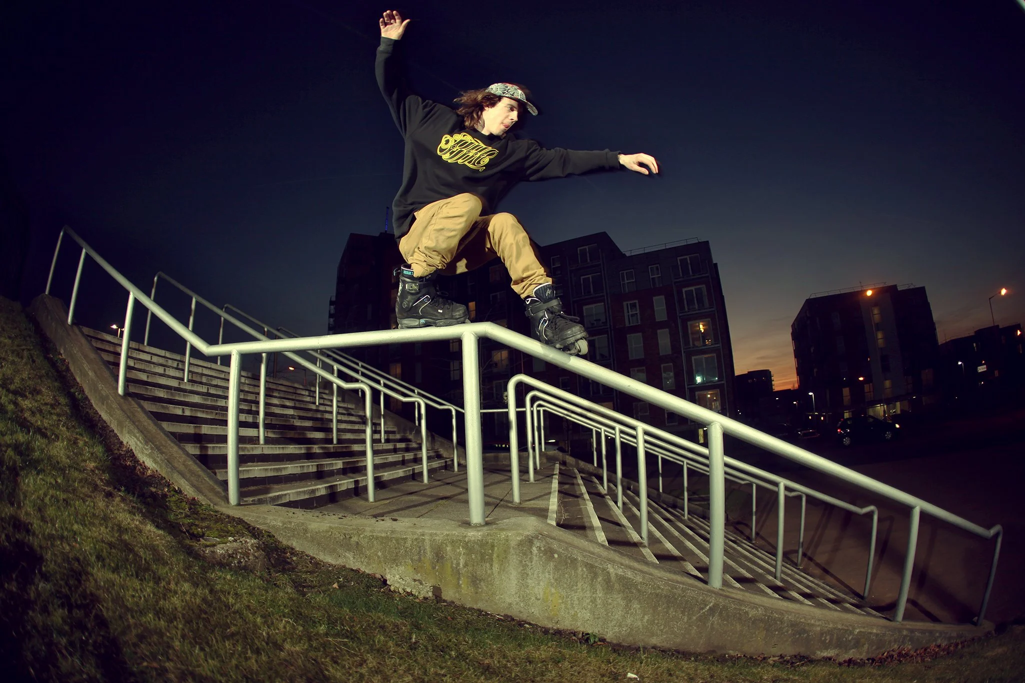 Skateboarder performing a trick on a rail at dusk in an urban area.