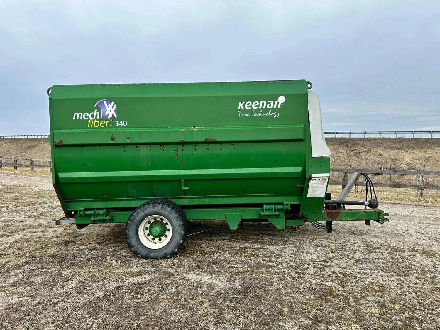 Right side profile view of a green used trailed Keenan MechFiber 340 horizontal TMR mixer wagon on a single axle in a field.