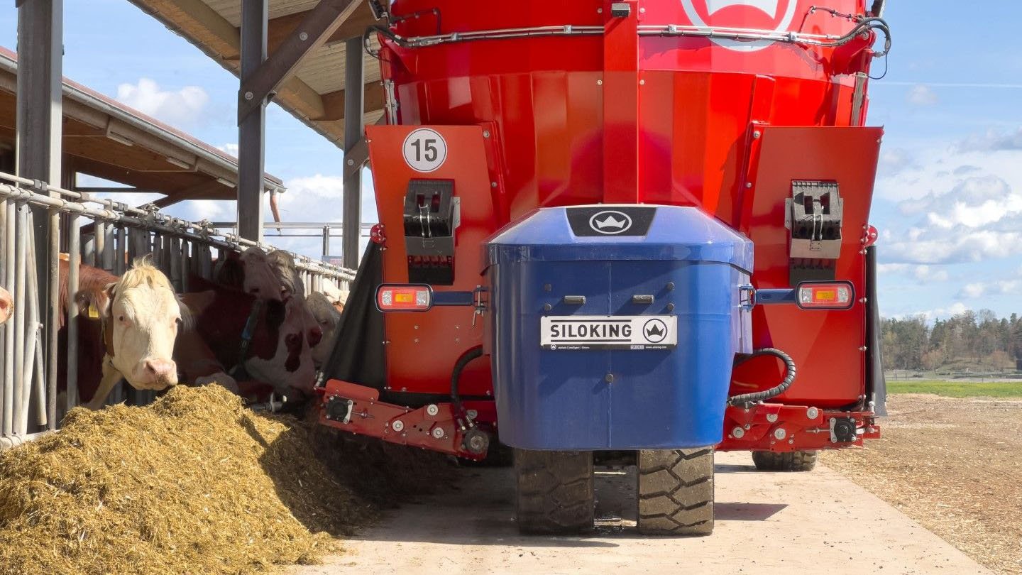 Rear view of a blue and red Siloking TruckLine eTruck 2012 zero-emission mixer distributing clean feed ration along a feed bunk barrier.