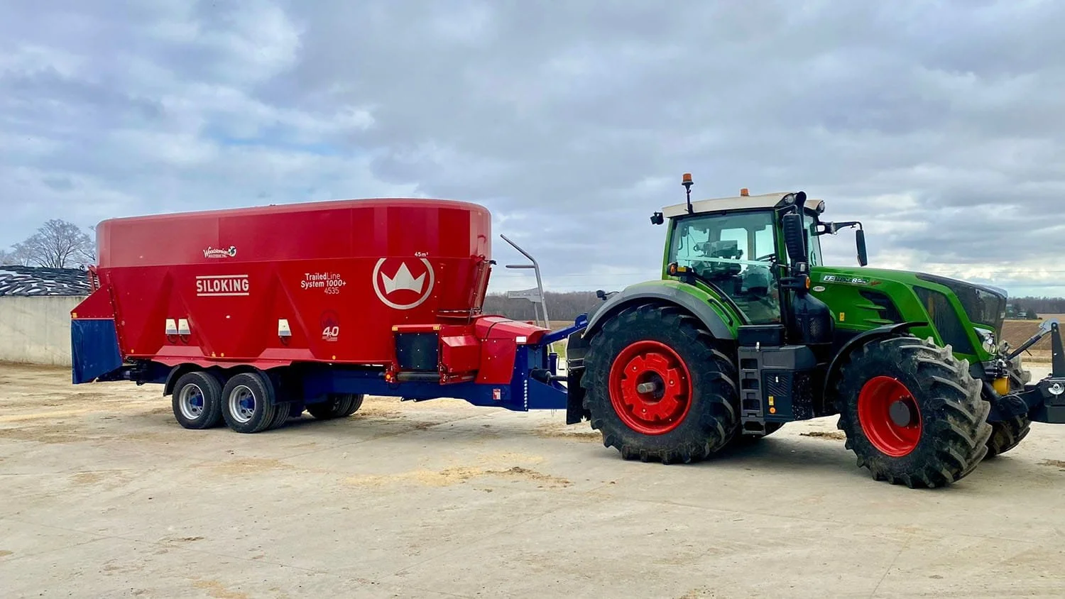 A red Siloking TrailedLine System 1000 plus 4535 vertical mixer wagon hitched to a green Fendt tractor in an open farm lot.