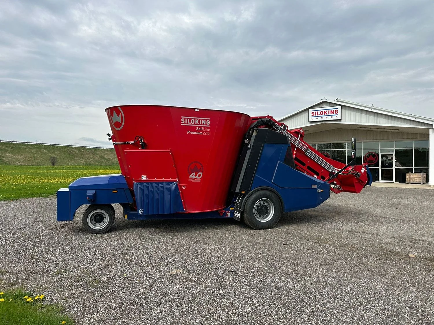 Right side profile view of a new red and blue Siloking SelfLine 4.0 Premium 2215-15 self-propelled vertical TMR feed mixer parked outside the Siloking Canada dealership building.