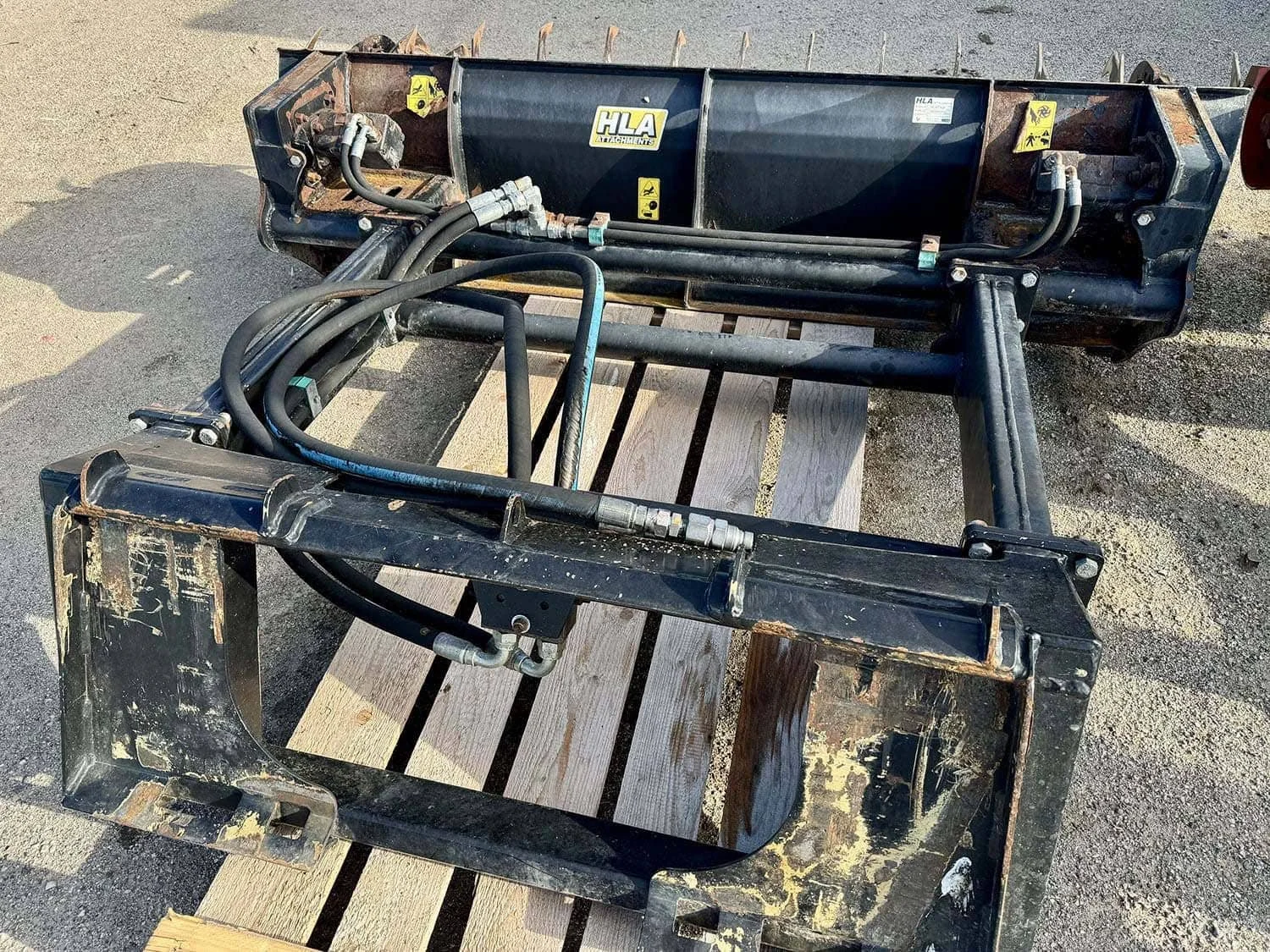 Rear view of a used HLA 84 inch silage facer attachment showing the universal skid steer quick-attach plate and hydraulic line routing.