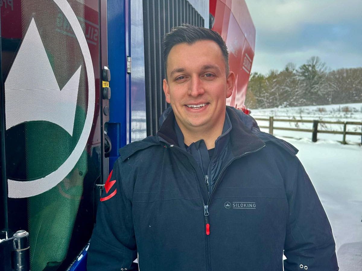 Dennys Pychnenko, Sales Team specialist at Siloking Canada, smiling outdoors in front of a blue and red cattle feed mixer during winter.