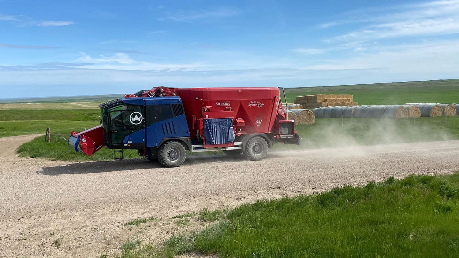 Side view of a Siloking SelfLine System 500 plus traveling down a gravel farm road leaving a trail of dust, demonstrating its independent air suspension and hight speed.