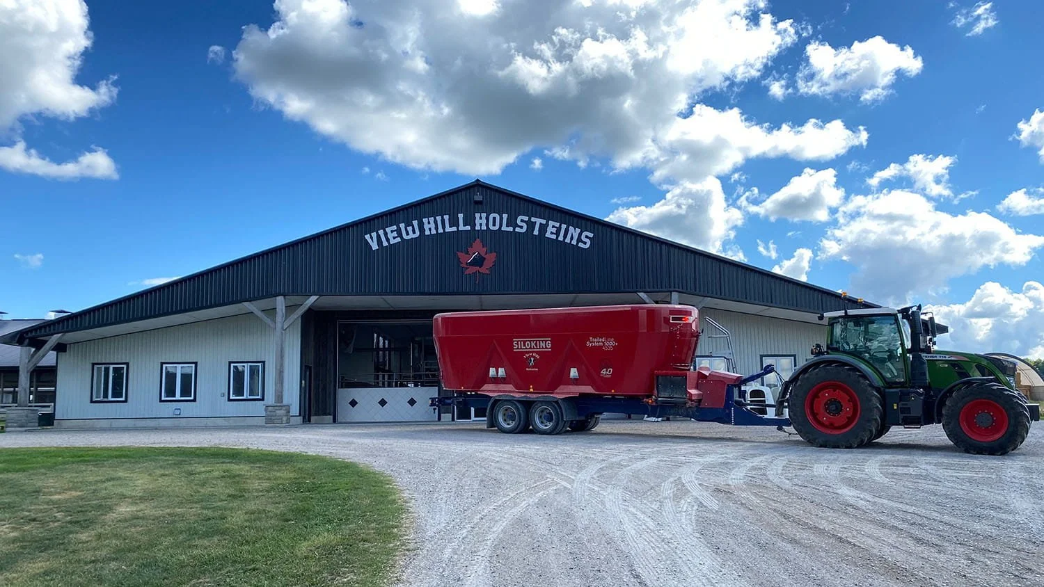 A green Fendt tractor hitched to a red Siloking TrailedLine System 1000 plus 4535 feed mixer parked in front of the View Hill Holsteins dairy barn.