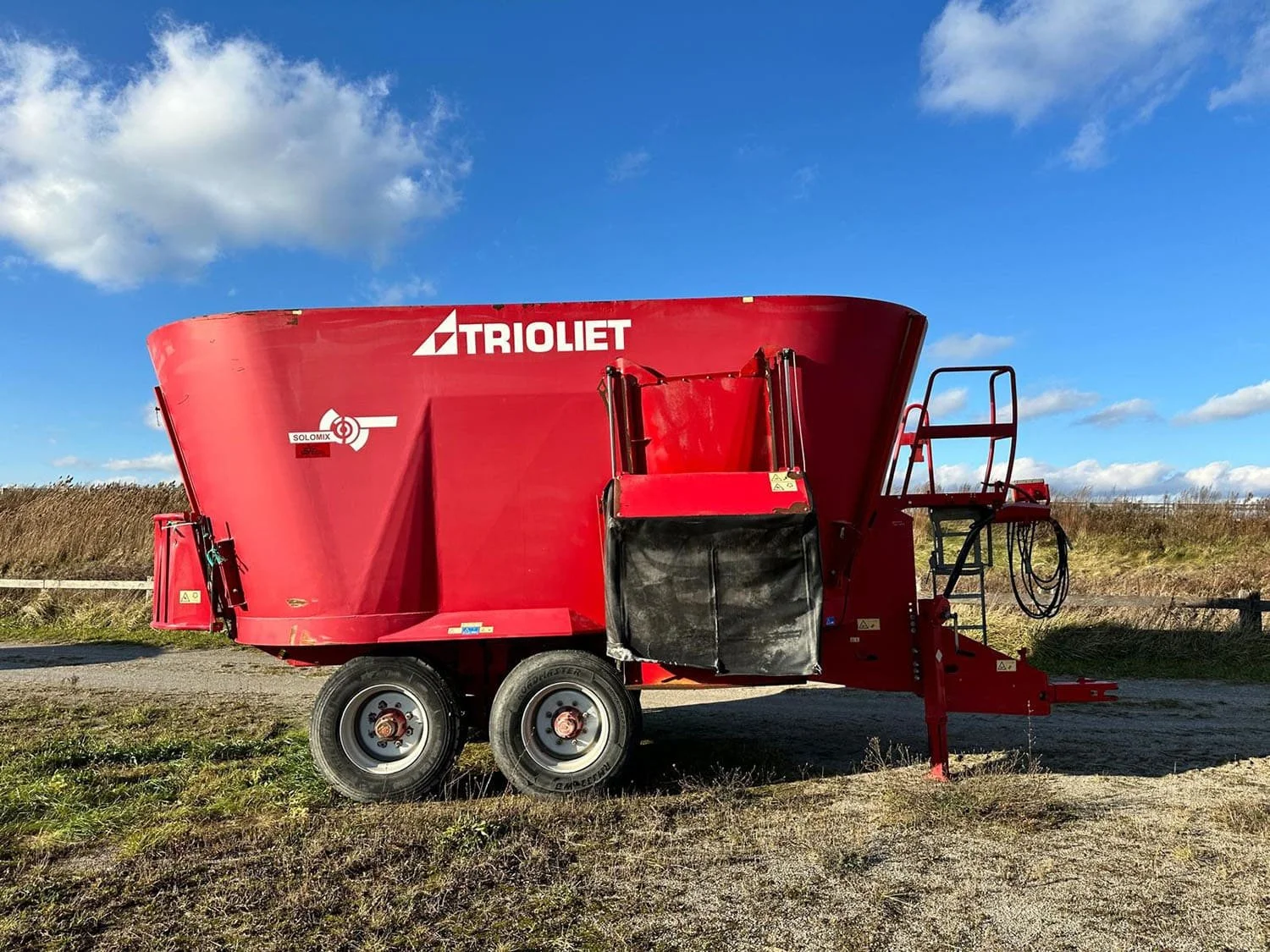 Used red 2016 Trioliet Solomix 2-2800 trailed vertical TMR feed mixer wagon side view showing front access ladder and side discharge door for sale at Siloking Canada.