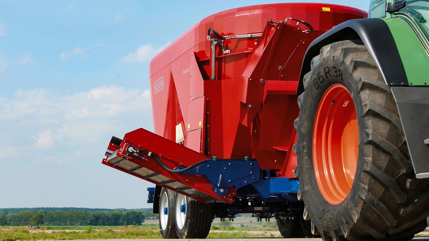 Close-up view of a Siloking TrailedLine vertical feed mixer conveyor discharge belt assembly next to a large tractor tire.