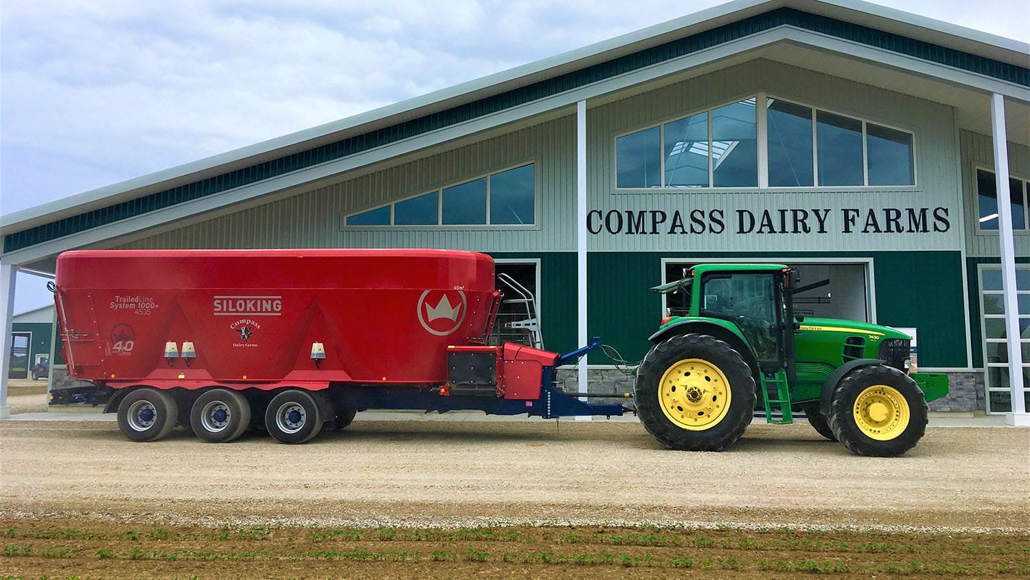 A green John Deere tractor hitched to a triple-axle 40 cubic meter Siloking TrailedLine System 1000 plus 4535 mixer wagon at Compass Dairy Farms.
