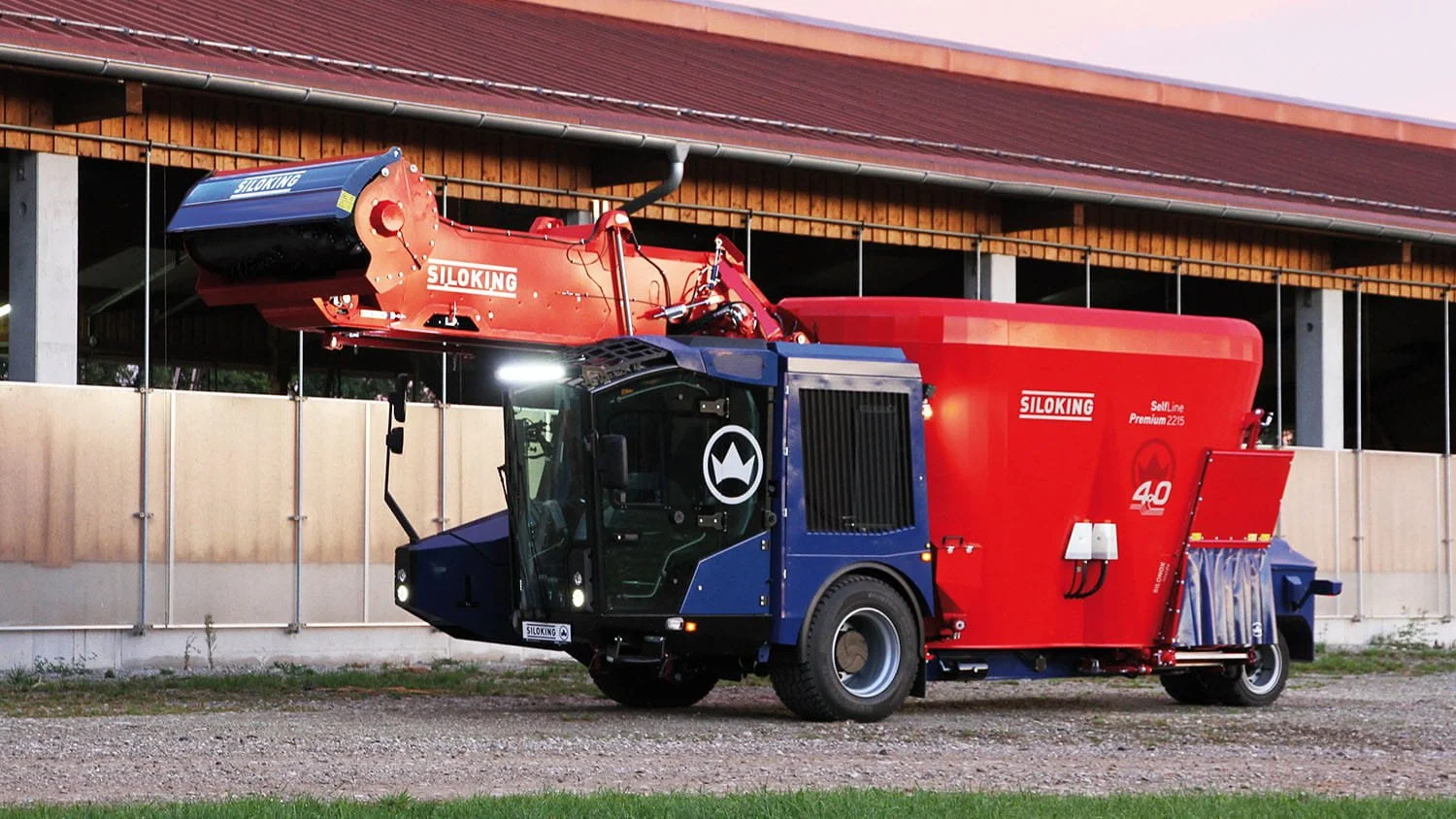 Side view of a Siloking SelfLine Premium self-propelled TMR mixer with its front milling cutter arm lowered, driving by dairy barn.