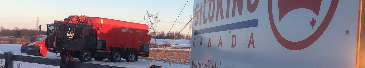 A wide panoramic view showing a red self-propelled mixer wagon parked next to the frosted fence line of the Siloking Canada facility showroom during a clear winter morning.