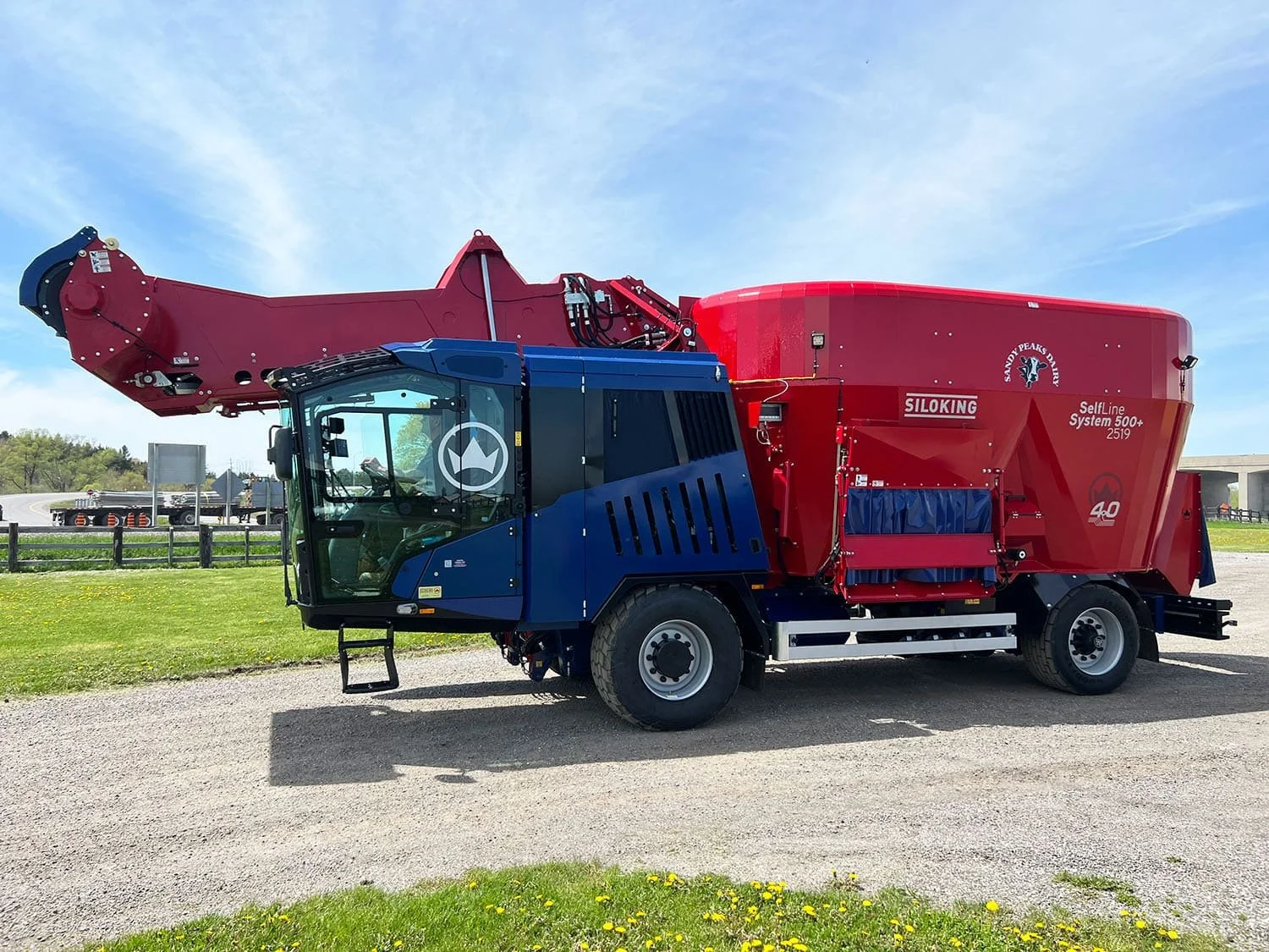 Left side profile view of a new red and blue Siloking SelfLine 4.0 System 500+ 2519-27 self-propelled vertical TMR feed mixer showing the high-reach silage milling loader arm fully raised.