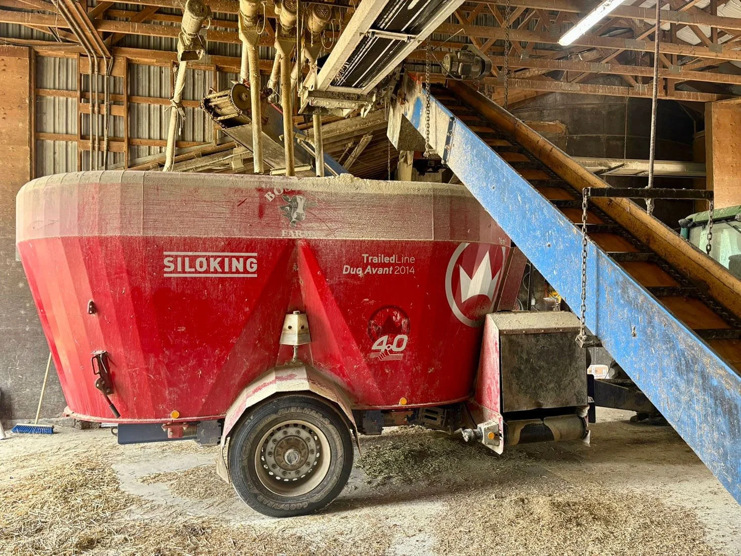 A red Siloking TrailedLine Duo Avant 2014 twin-auger mixer wagon positioned under a barn conveyor loading system on a Canadian farm.