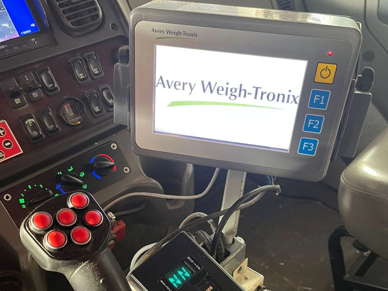 Interior cab view showing the main multi-button control joystick, Allison automatic transmission pad, and an Avery Weigh-Tronix scale monitor display
