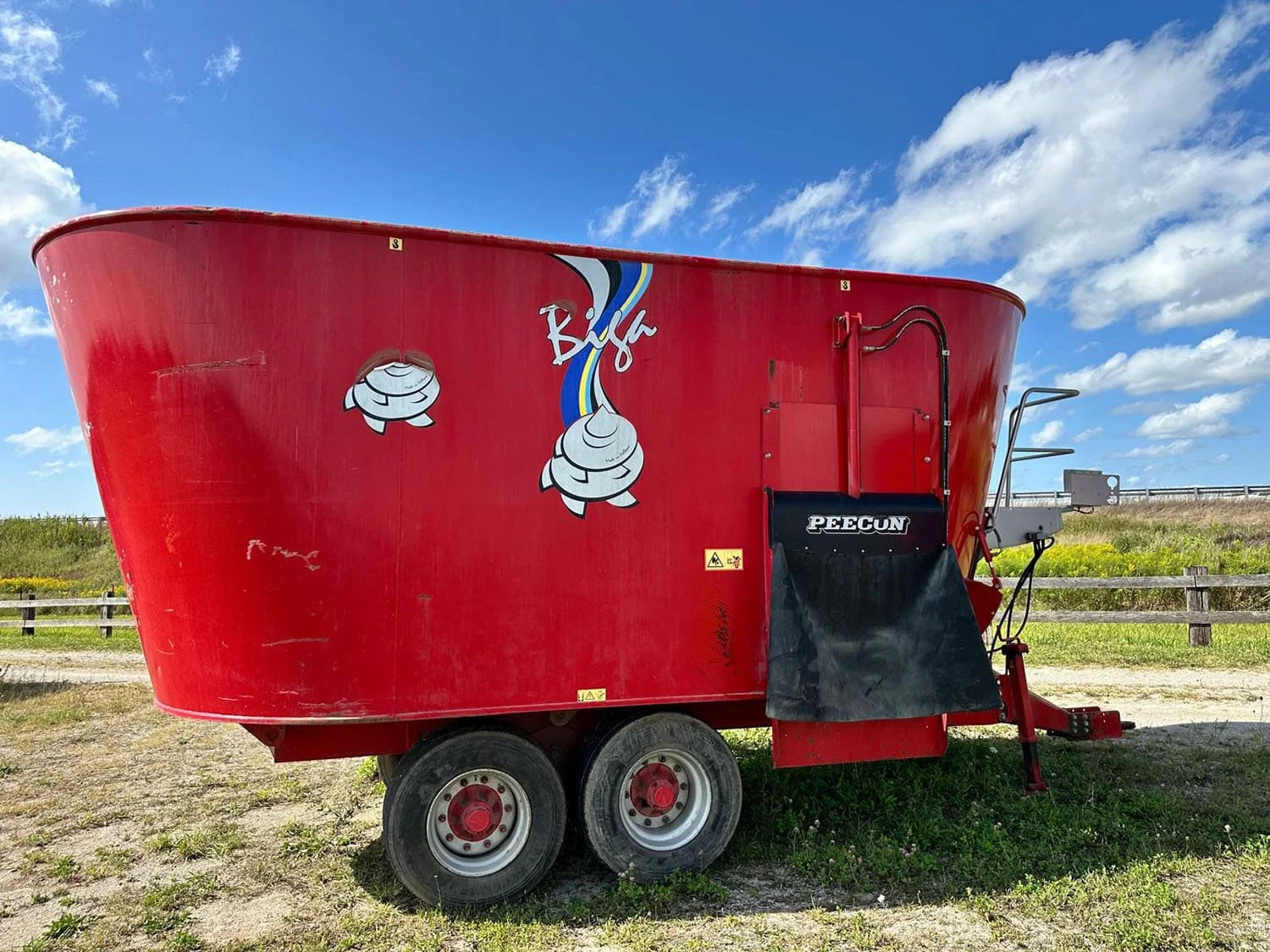 Right side profile view of a used red Peecon VME 300 twin auger vertical TMR mixer wagon on a tandem axle.