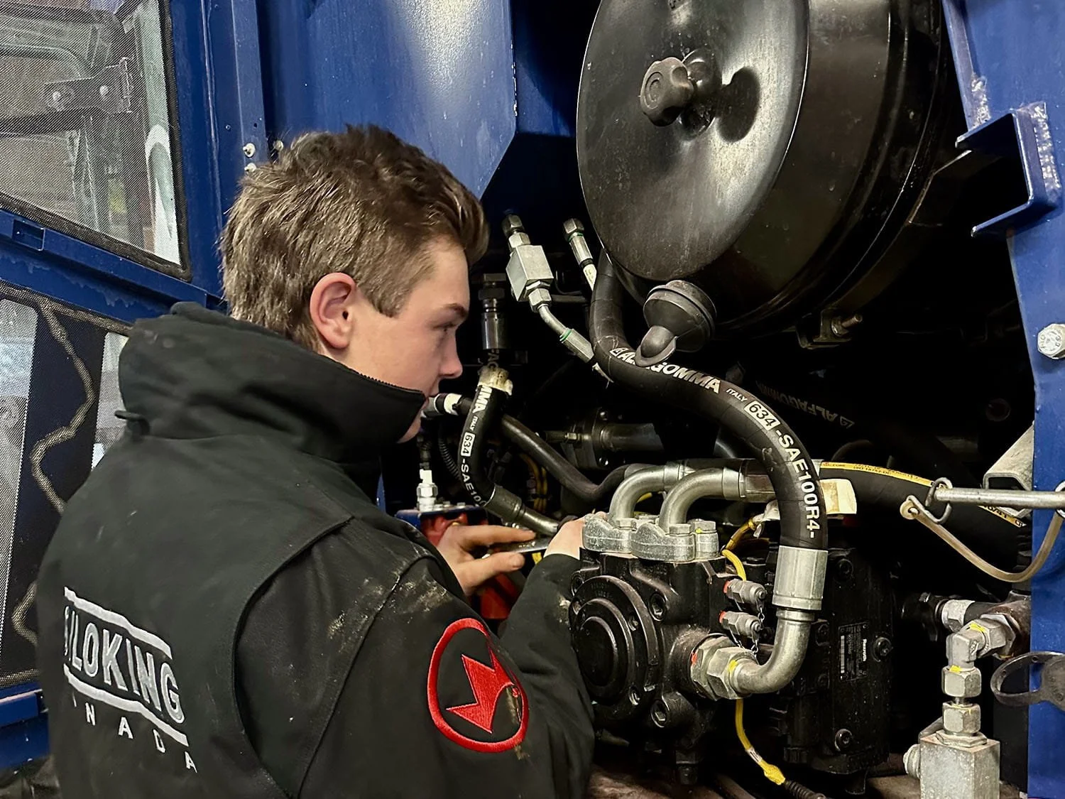 Close-up view of an equipment technician working on the complex hydraulic pump and engine components of a self-propelled TMR mixer wagon.