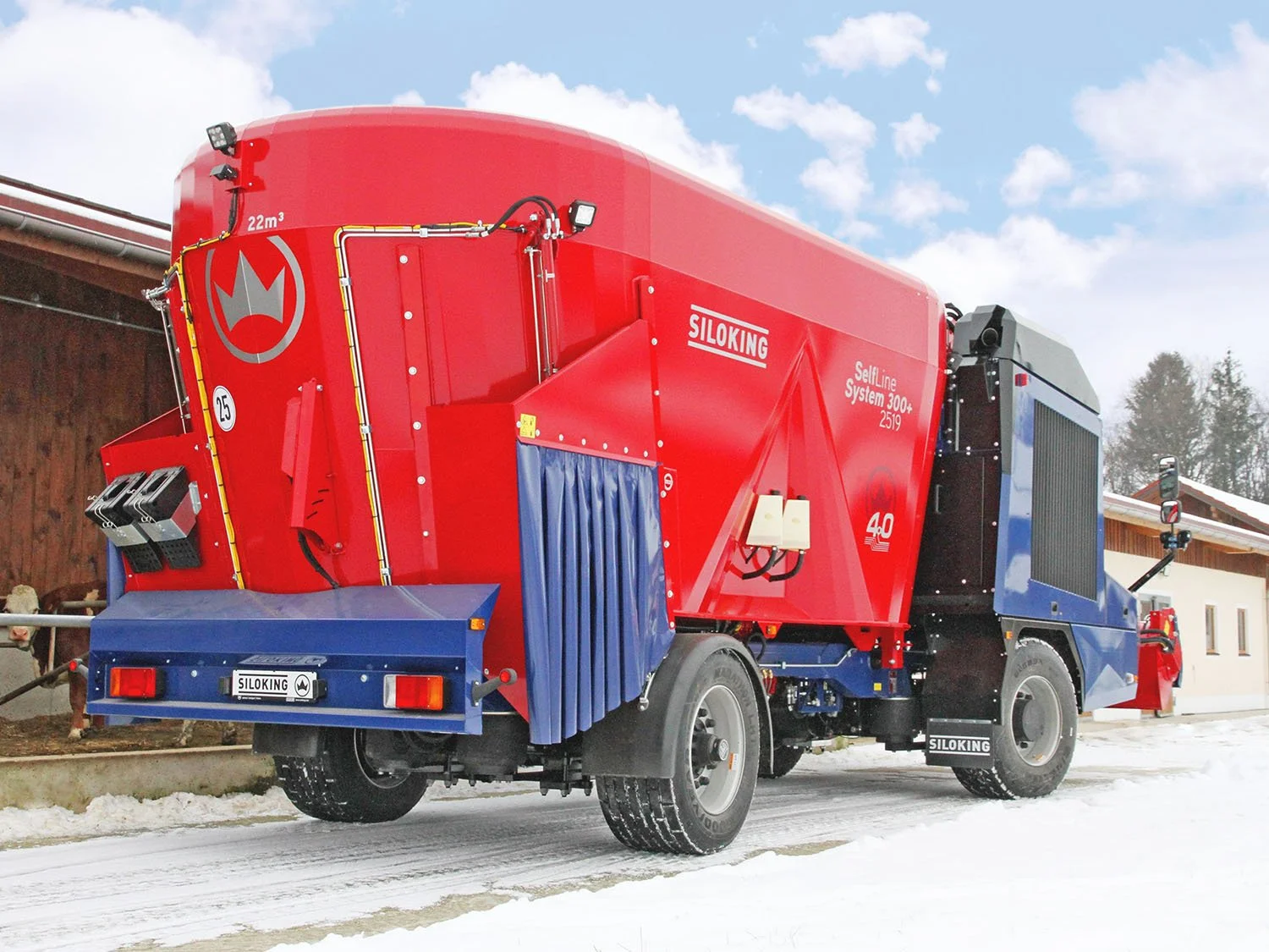 Rear three-quarter view of a high-capacity red and blue Siloking SelfLine System 300 plus 2519 self-propelled vertical feed mixer operating on a dairy farm in winter.