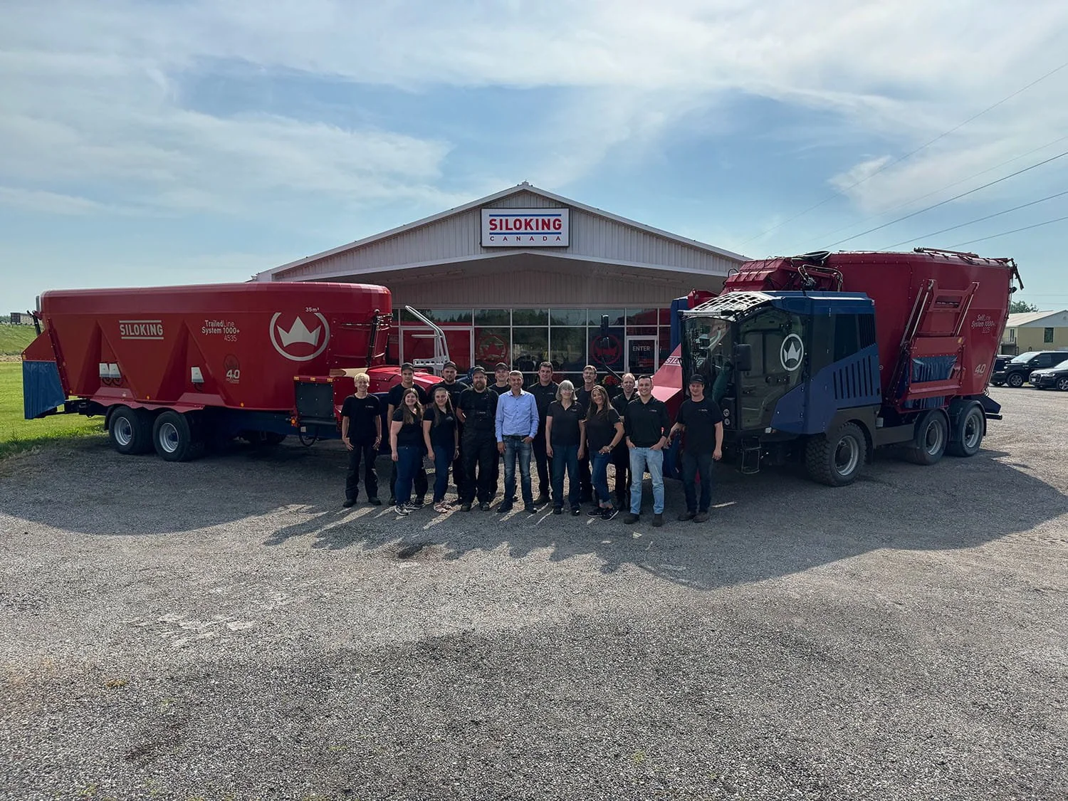 Group portrait of the Siloking Canada team, flanked by a TrailedLine mixer on the left and a SelfLine 4.0 mixer on the right, with the main facility building and logo visible in the background.