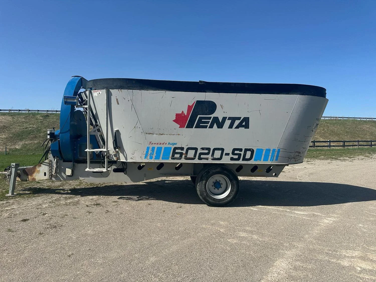 Right side view of a grey used Penta 6020-SD vertical feed mixer wagon on a single axle showing the front right discharge door and access ladder steps.