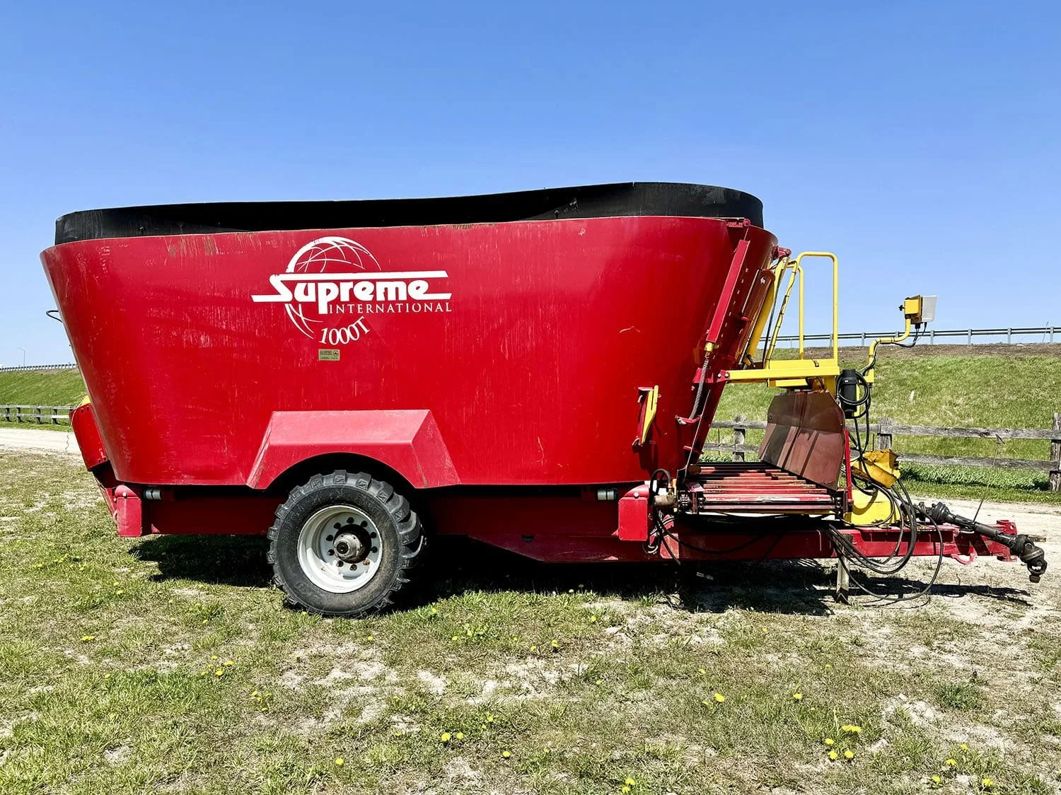 Right side view of a red used Supreme International 1000T twin auger vertical mixer wagon on a single axle showing the front cross conveyor assembly.