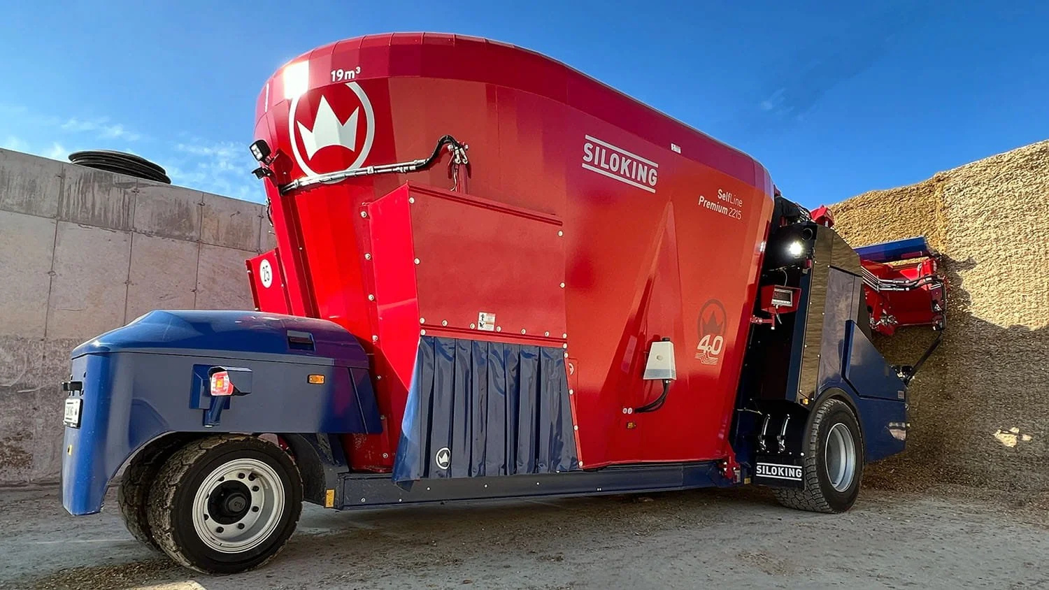 Rear three-quarter view of a red and blue Siloking SelfLine Premium 2215 19 cubic meter self-propelled TMR feed mixer operating next to a concrete silage bunker.
