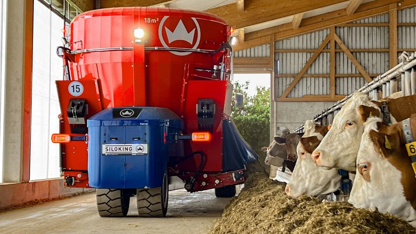 An 18 cubic meter Siloking TruckLine eTruck 2012 electric mixer discharging fresh total mixed ration silently to dairy cattle along an indoor feed alley.