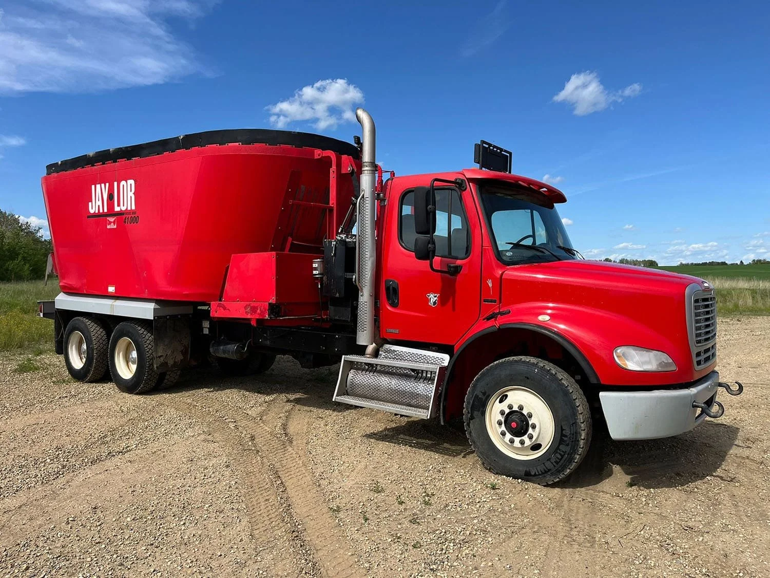 Front right three-quarter view of a red Jaylor TM41000 commercial truck mixer showing the side exhaust stack and front cross conveyor setup.