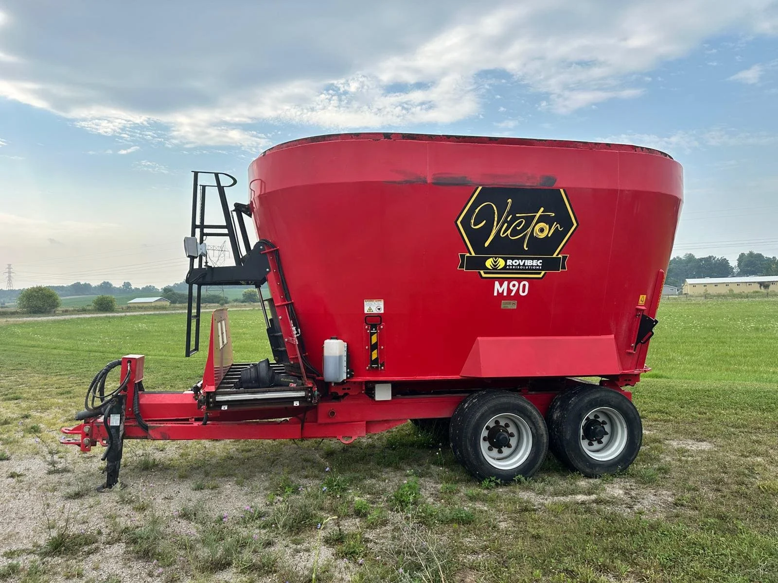 Used red Rovibec Victor M90 trailed vertical TMR feed mixer wagon side profile view with front cross conveyor for sale at Siloking Canada.