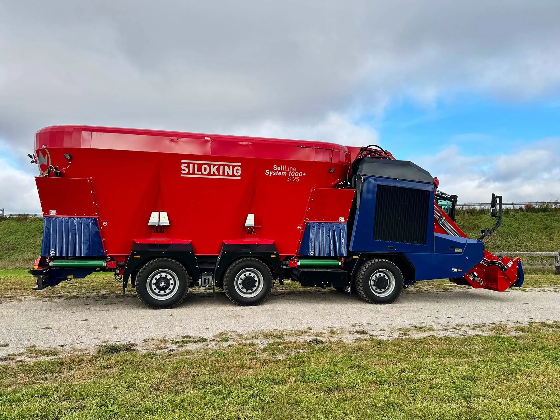 Right side profile of a red and blue Siloking SelfLine System 1000+ 3225 self-propelled TMR mixer with tridem axles.