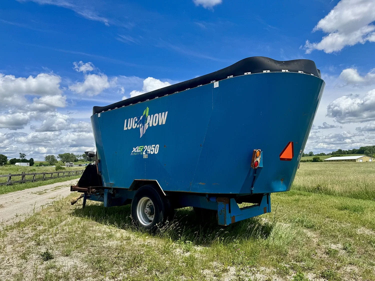 Rear three-quarter view of a blue Lucknow XLR2950 vertical TMR mixer wagon with tub extension parked in a grassy field.