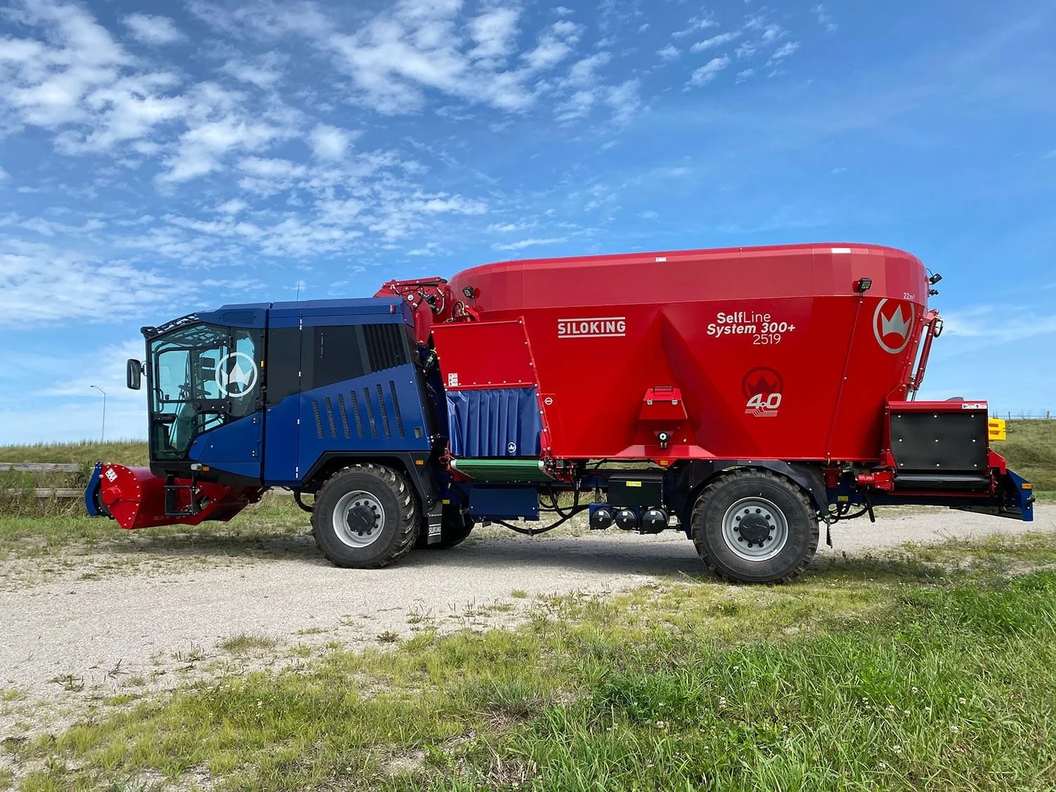 Left side profile view of a new red and blue Siloking SelfLine 4.0 System 300+ 2519-22 4x4 self-propelled vertical TMR feed mixer parked outside.