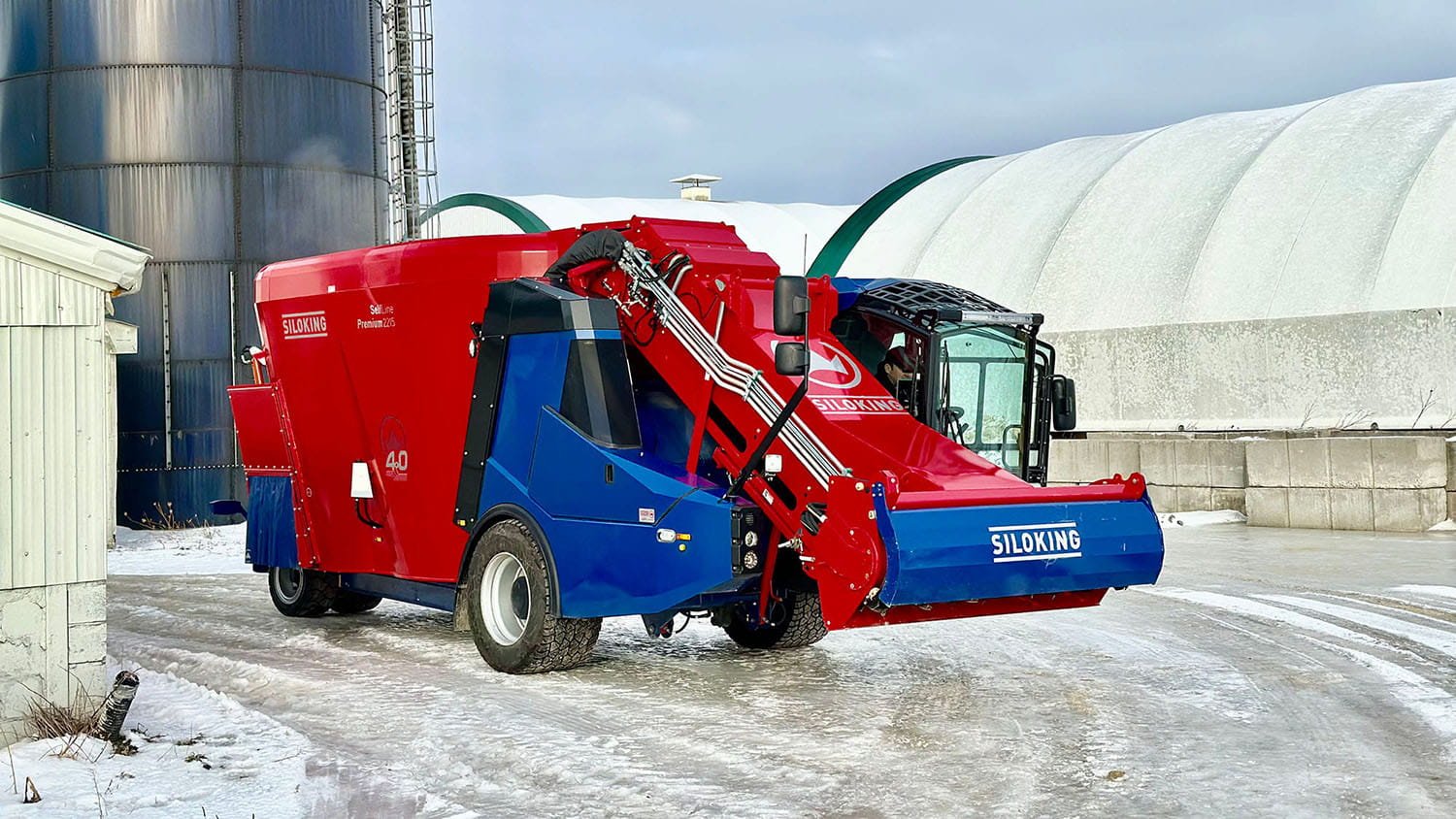 A red and blue Siloking SelfLine Premium 4.0 operating on a snow-cleared path next to silage storage domes on an Ontario farm in winter.