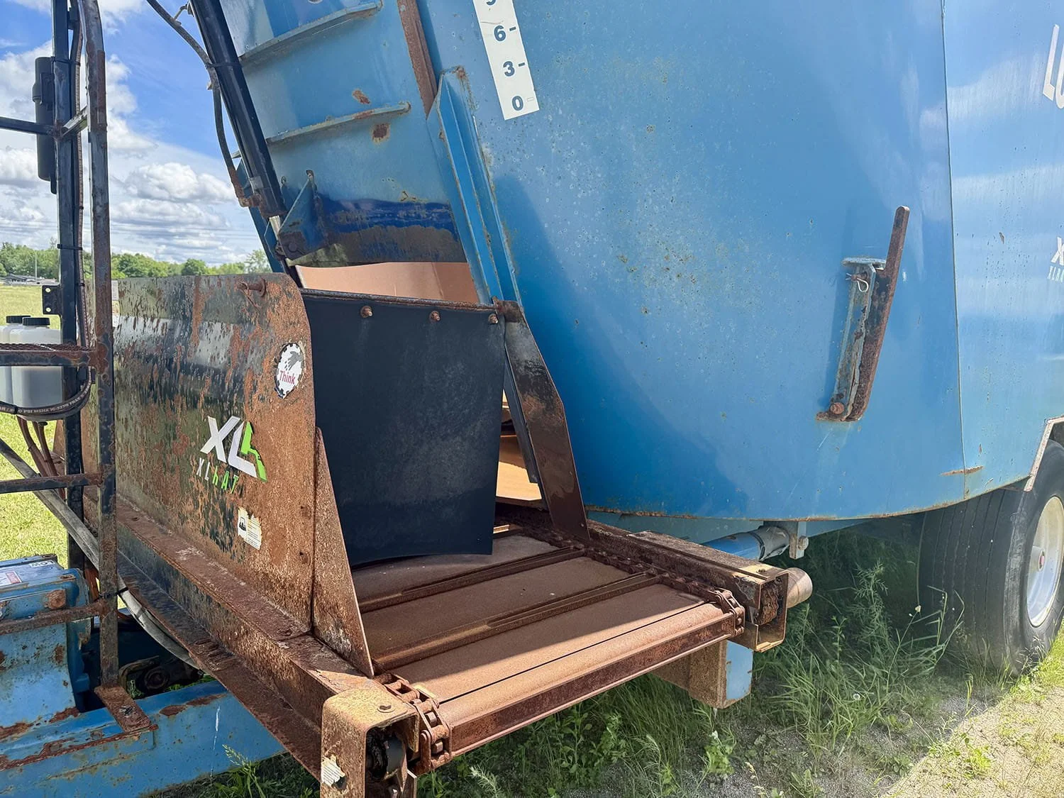 Close-up view of the front cross conveyor system and discharge door on a blue Lucknow XLR2950 vertical mixer wagon.