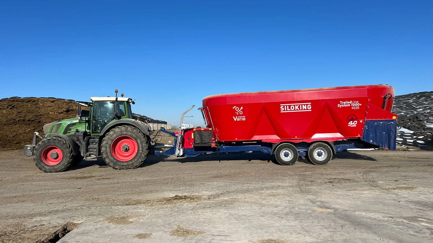 A high-capacity red Siloking TrailedLine System 1000 plus 4535 vertical mixer wagon featuring the Vario transmission logo, hitched to a green Fendt tractor in front of outdoor silage bunker piles.