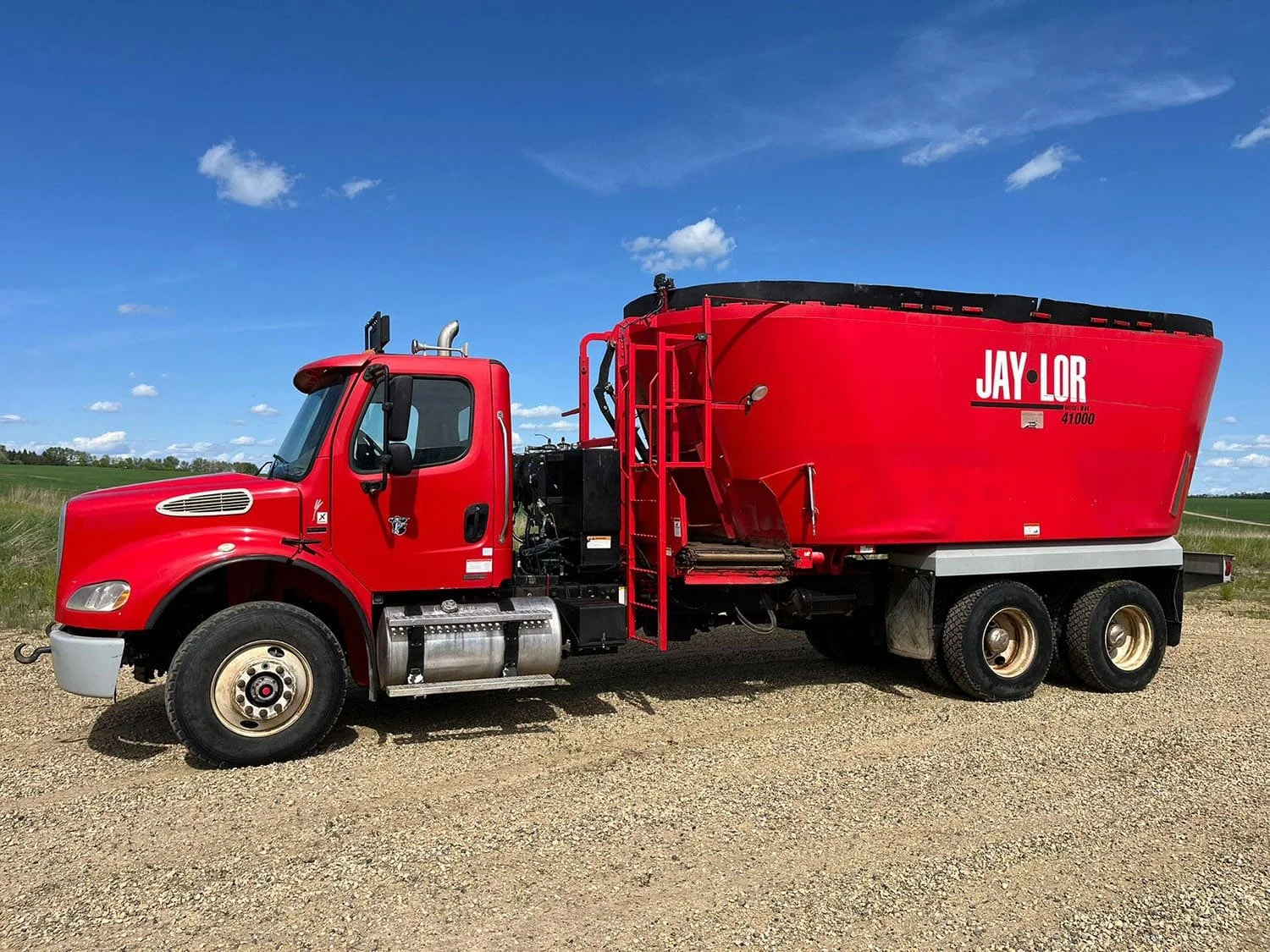 Full left side profile view of a red Jaylor TM41000 truck-mounted vertical mixer showing the front cross conveyor discharge system and service ladder.