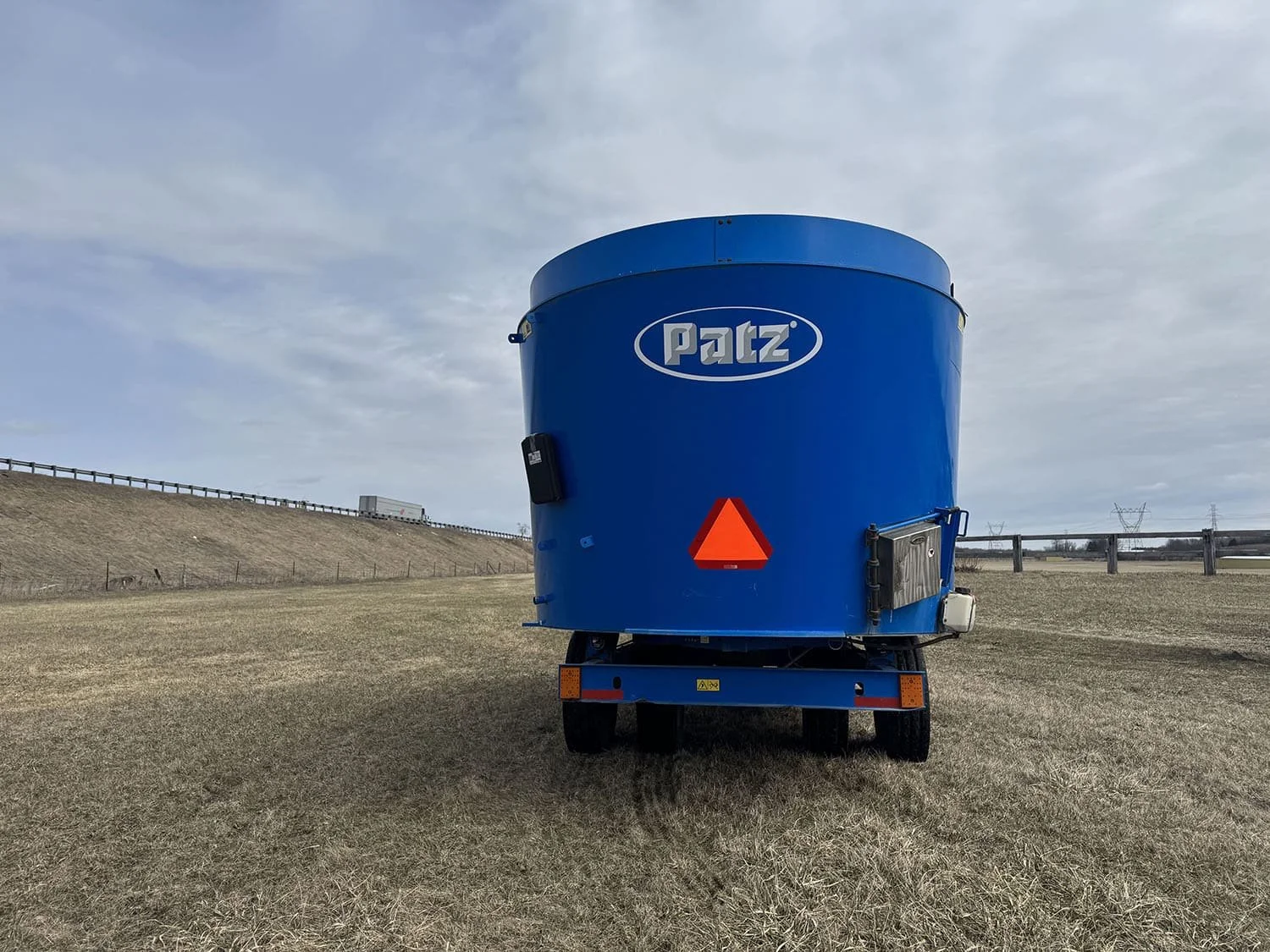 Rear view of a blue used Patz 2400 Series II 650XH vertical feed mixer showing transport tires and slow moving vehicle sign.