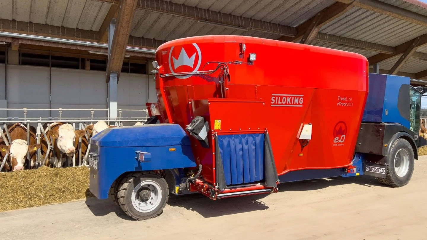 Three-quarter view of a battery-powered Siloking TruckLine eTruck 2012 self-propelled mixer wagon feeding dairy cows under a covered barn awning.