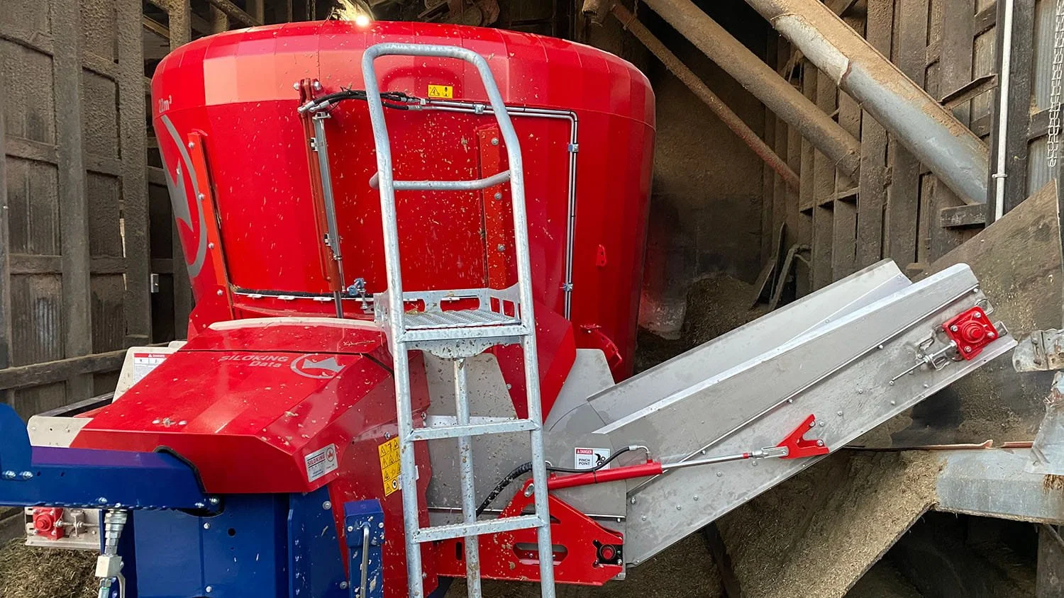 Close-up view of a custom-fabricated front cross conveyor system with an adjustable elevator extension mounted on a red Siloking TrailedLine mixer wagon.
