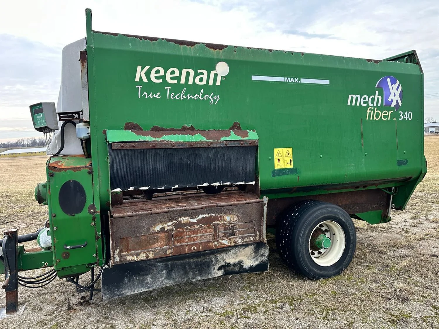 Left side view of a green used Keenan MechFiber 340 horizontal paddle TMR feed mixer wagon showing the side discharge chute assembly for sale at Siloking Canada.