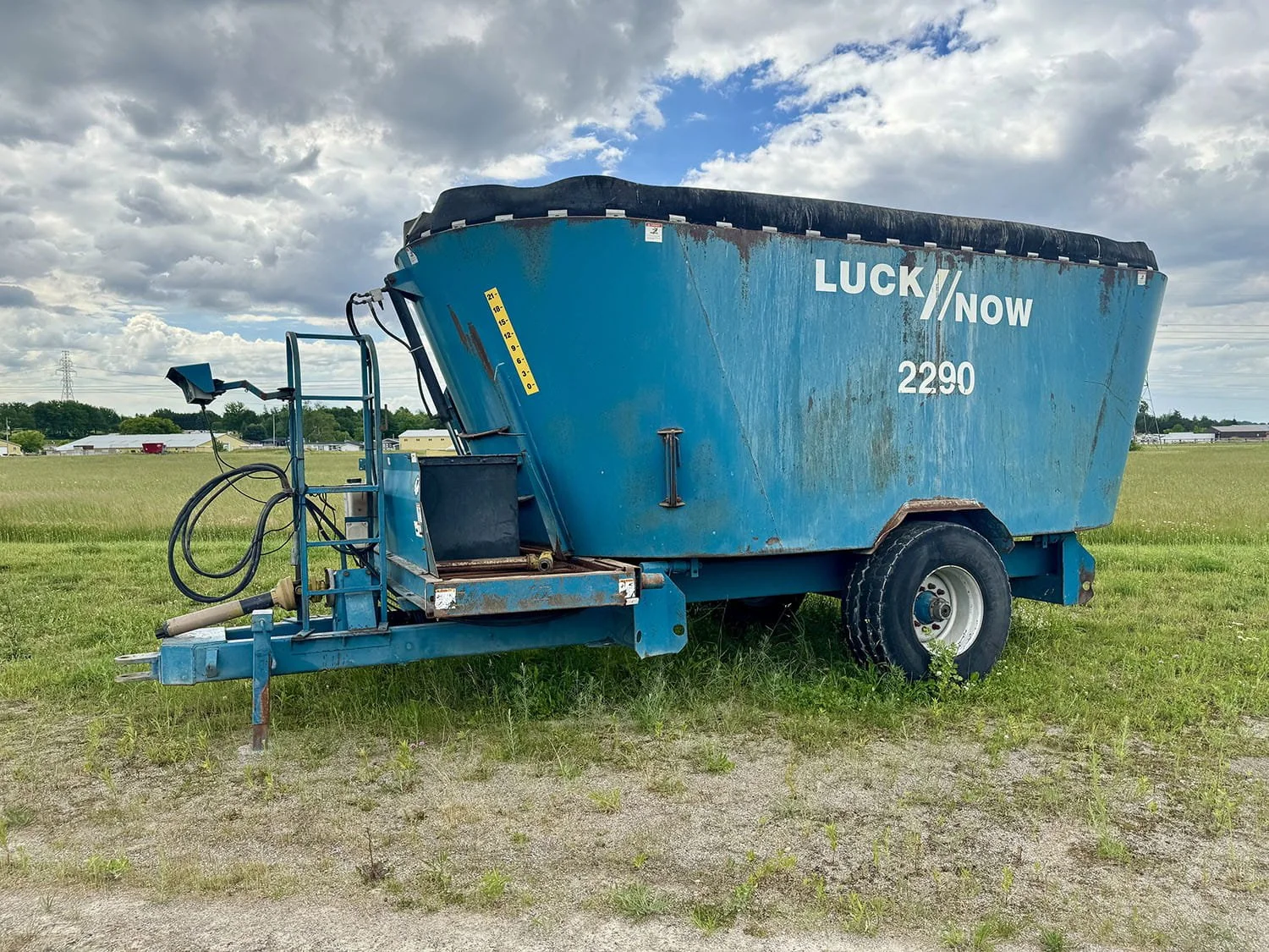 Right three-quarter view of a blue Lucknow 2290 vertical mixer wagon with rubber tub extension parked on grass under a cloudy sky.
