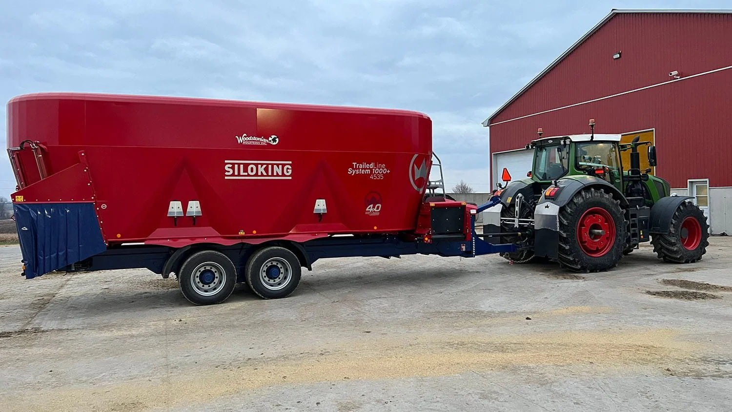 Side profile view of a Siloking TrailedLine System 1000 plus 4535 triple-auger mixer wagon and Fendt tractor parked by a large red dairy barn.