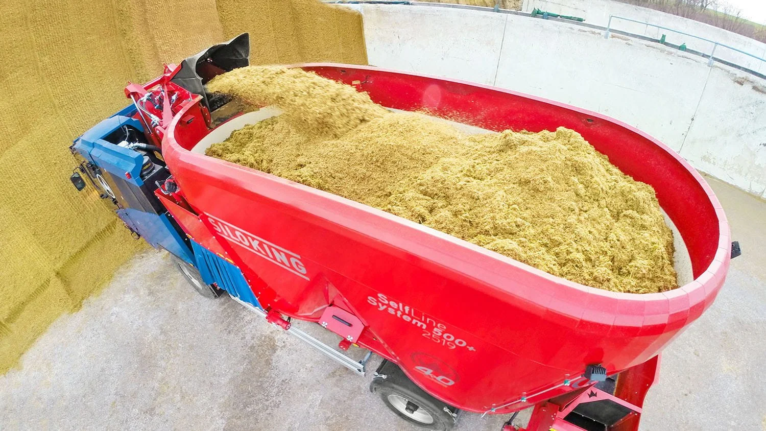 Wide aerial drone image looking directly down into the large open twin-auger mixing tub of a Siloking SelfLine System 500 plus as it fills with 
silage.