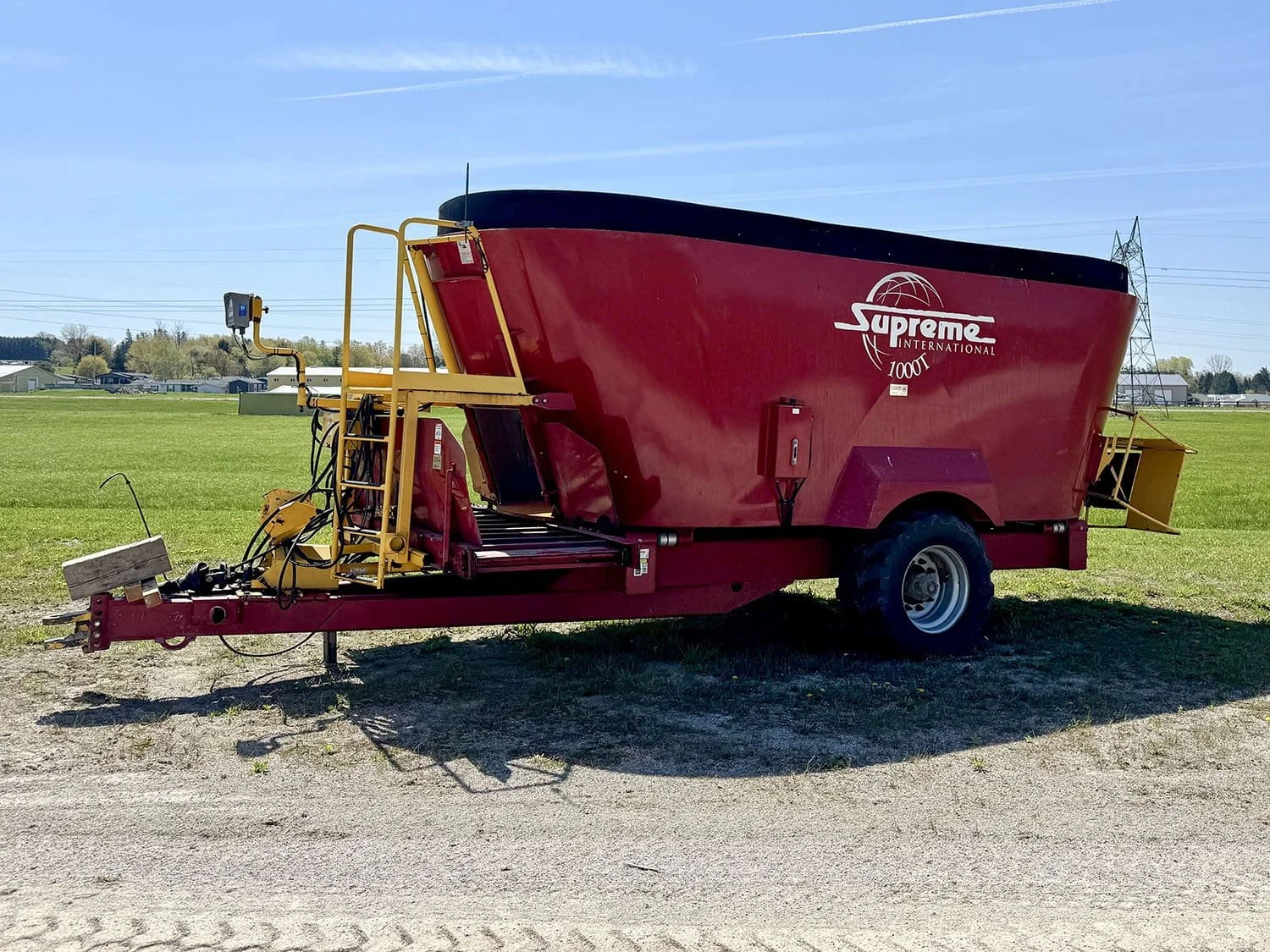 Left side profile view of a red used Supreme International 1000T trailed vertical TMR feed mixer wagon featuring floatation tires and a front access ladder for sale at Siloking Canada.