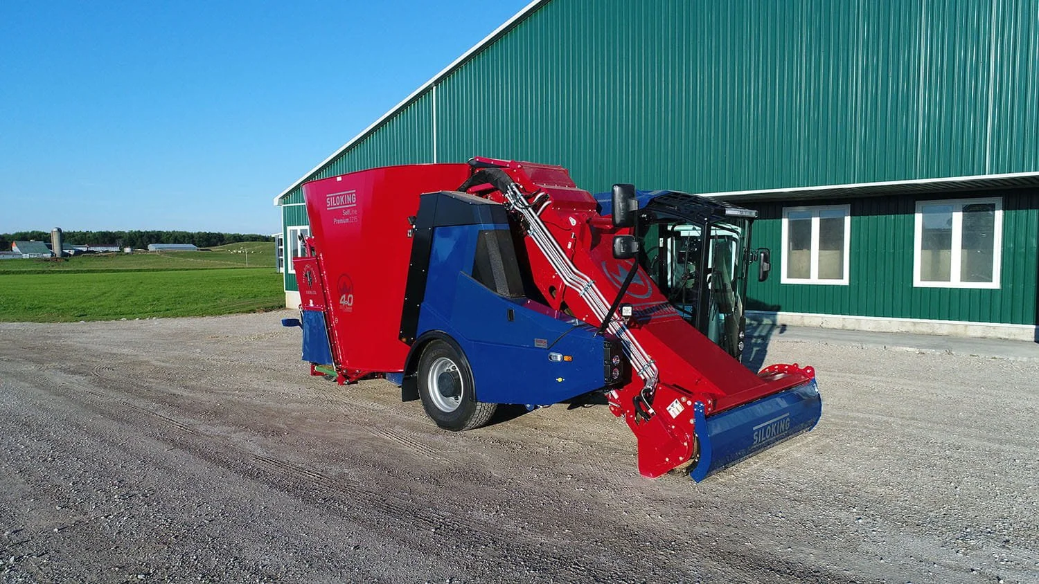 Wide-angle profile shot of a Siloking SelfLine Premium 4.0 vertical self-propelled feed mixer parked on a gravel lot next to a green farm utility building.
