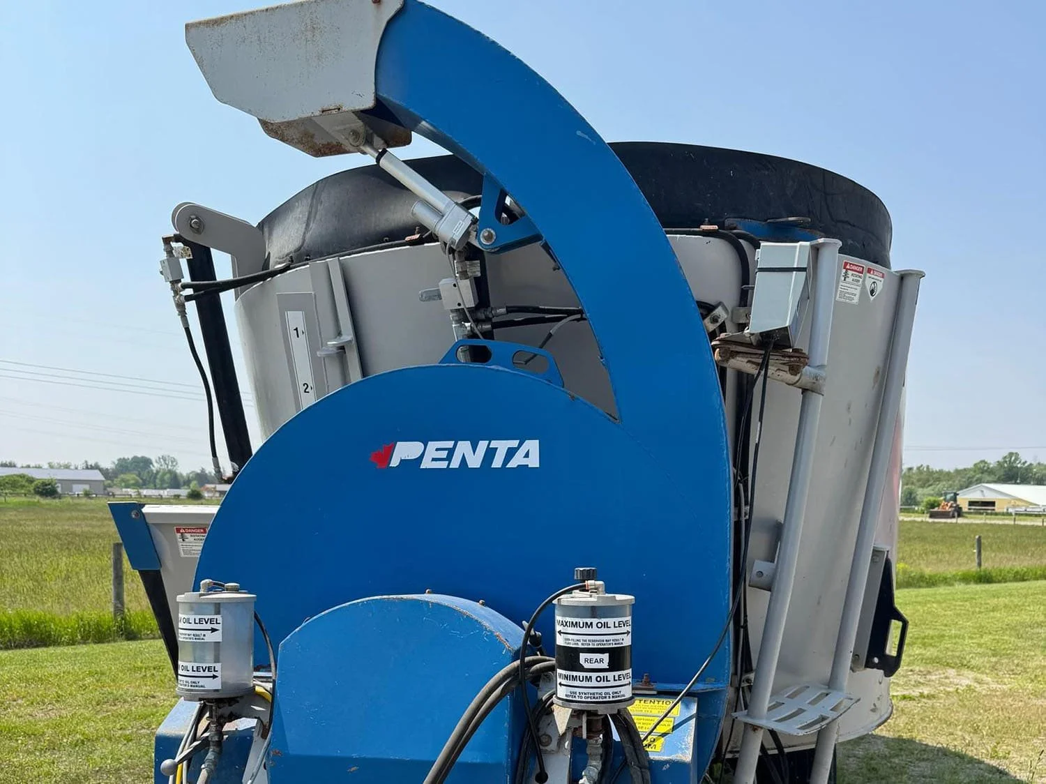 Close-up front view of the blue factory front-mounted straw bedding blower chute assembly and hydraulic oil reservoir tanks on a Penta vertical mixer wagon.