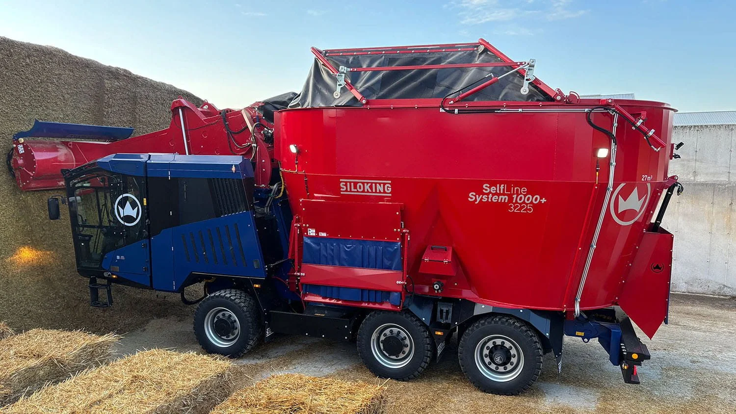 Side profile of a red Siloking SelfLine System 1000 plus using its front milling head to cleanly extract feed from a concrete bunker silo face.