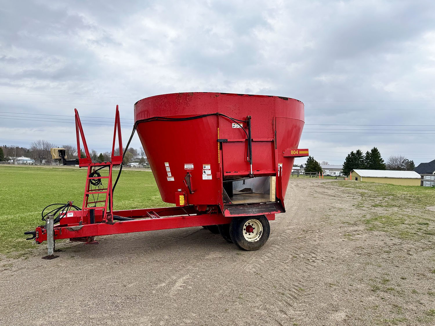 Left side profile view of a red used 2014 NDE 804 trailed single auger vertical TMR feed mixer wagon showing the left side discharge door for sale at Siloking Canada.