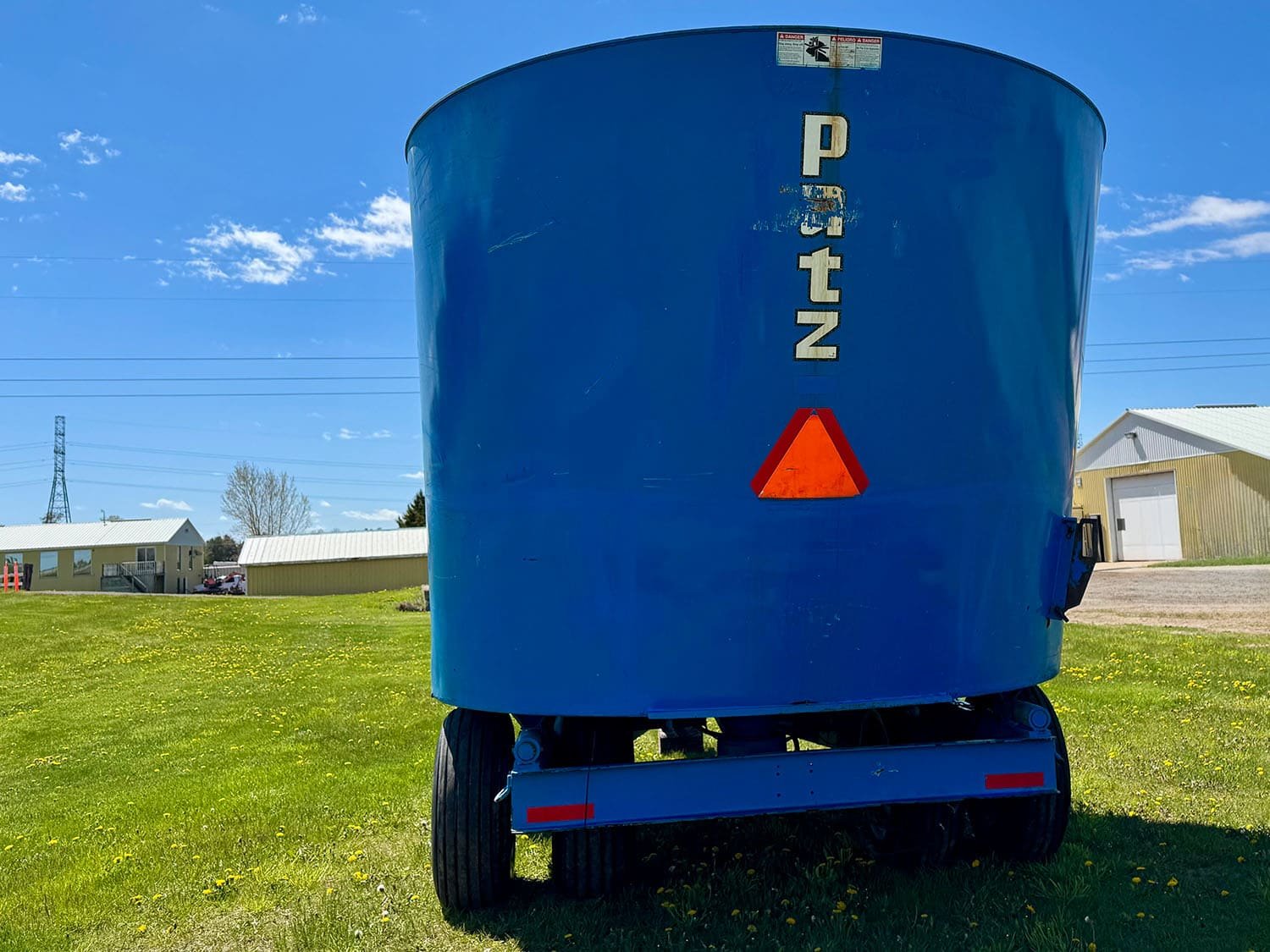Rear view of a blue used Patz V615 pull type vertical feed mixer wagon showing transport tires and slow moving vehicle sign.