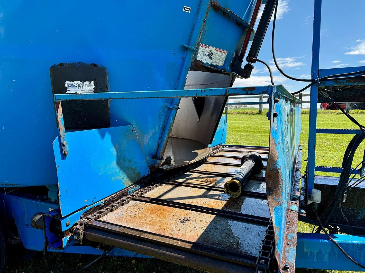 Detailed close-up view of the front cross conveyor discharge chain assembly and hydraulic door opening on a blue Patz TMR mixer.